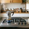 ガスコンロで抽出中のマキネッタと散らばったコーヒー豆のある朝の温かいキッチン風景