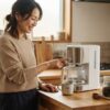 朝のキッチンで電動コーヒーメーカーのボタンを押す女性