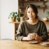 朝の明るいキッチンで温かなコーヒーカップを両手で持ち寄せる日本人女性