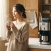 朝の明るいキッチンで電動コーヒーメーカーから淹れたコーヒーを楽しむ日本人女性の生活風景