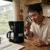 朝の日差しが入る日本のキッチンで、男性が象印コーヒーメーカーの型番ラベルを虫眼鏡で確認している様子。