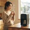 朝の日差しが差し込むキッチンで、Tigerコーヒーメーカーを背景に、淹れたてのコーヒーを両手で持ち満足げに微笑む日本人女性。